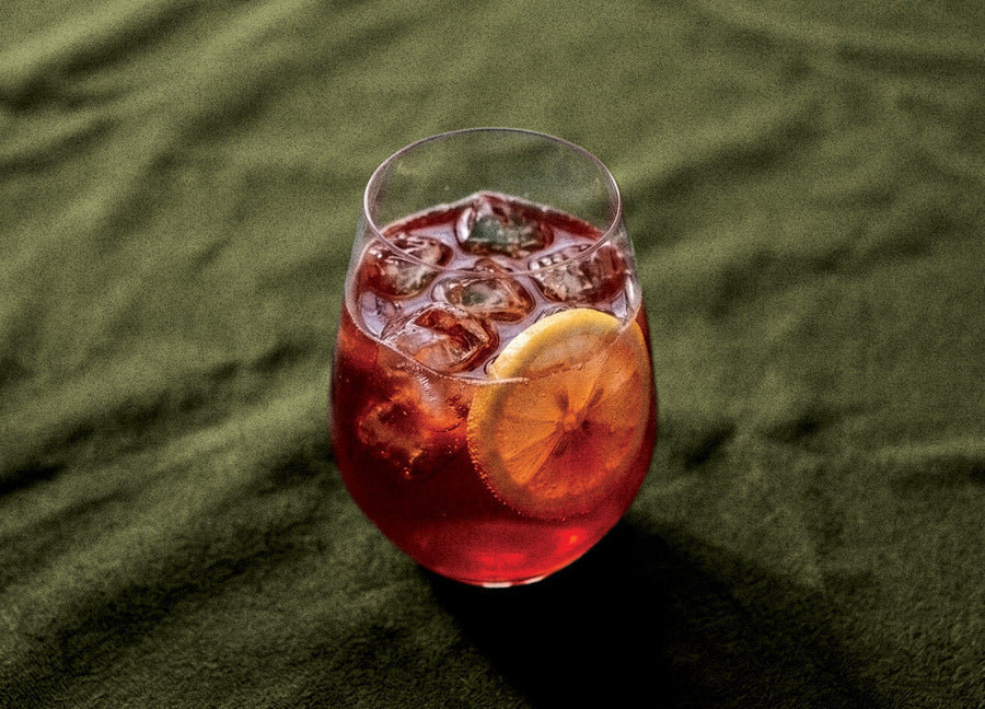Sloe-Nade-o cocktail made with Humdinger Sloe Gin, deep red over ice with a lemon wheel on green linen